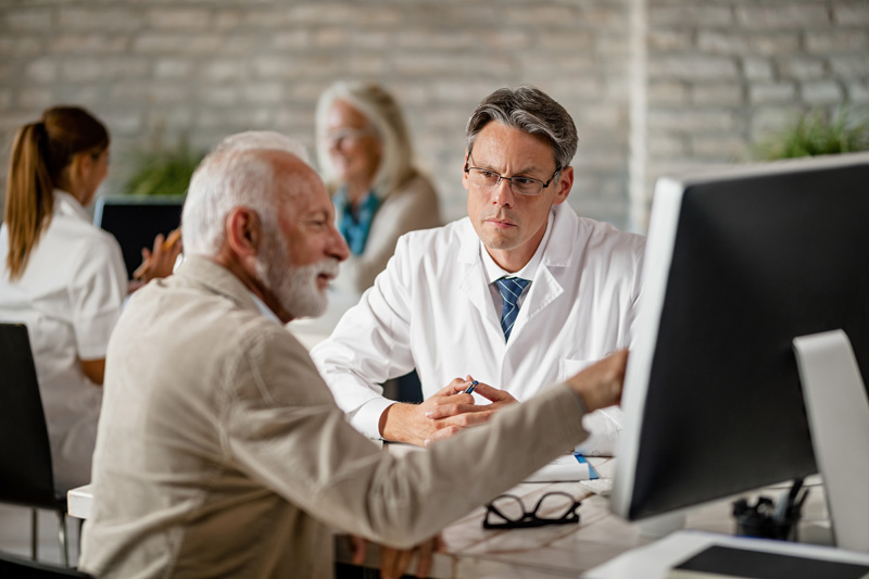 doctor and mature patient discussing about medical records on computer during consultations at clinicjpg