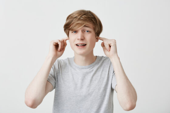 stressful man with trendy hairdo dressed casually plugs ears avoids loud sounds doesn t want hear noise 1 560x373jpg