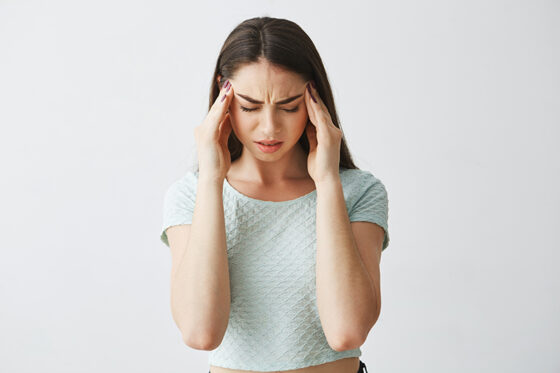 young beautiful brunette girl frowning touching temples headache isolated white background 1 560x373jpg