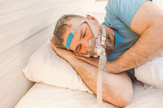 sleeping man with chronic breathing issues using cpap machine bed 560x373jpg